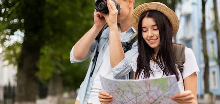 Imagem de um home e uma mulher, O homem está tirando fotografias de um ponto turístico, enquanto a mulher olha um mapa para ver qual será o próximos destino